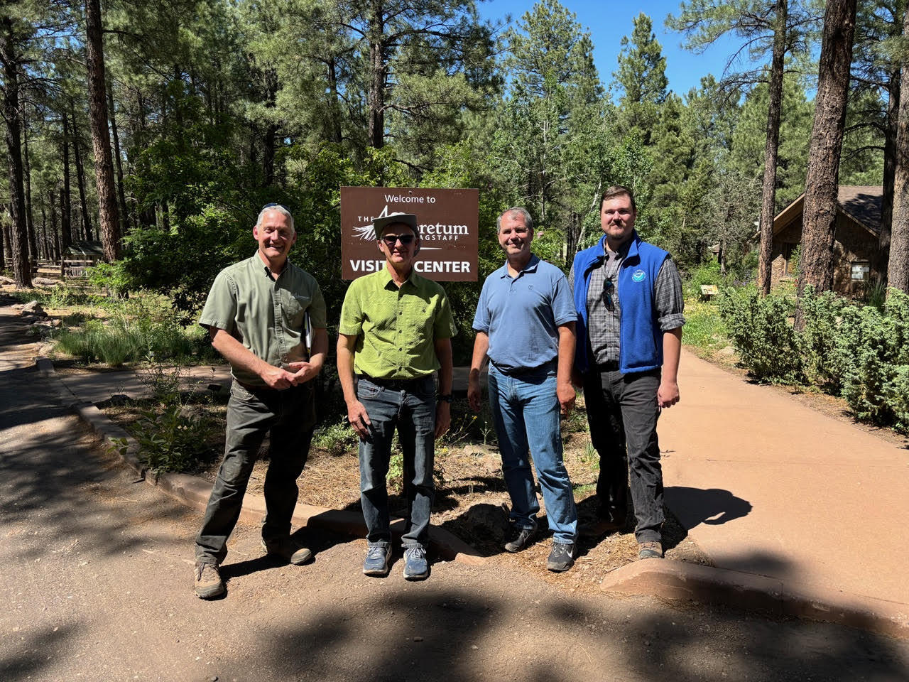 Scientists survey a possible observation site near Flagstaff, Arizona for fire weather. Photo shows four men on a dirt road in a forest of pine trees.