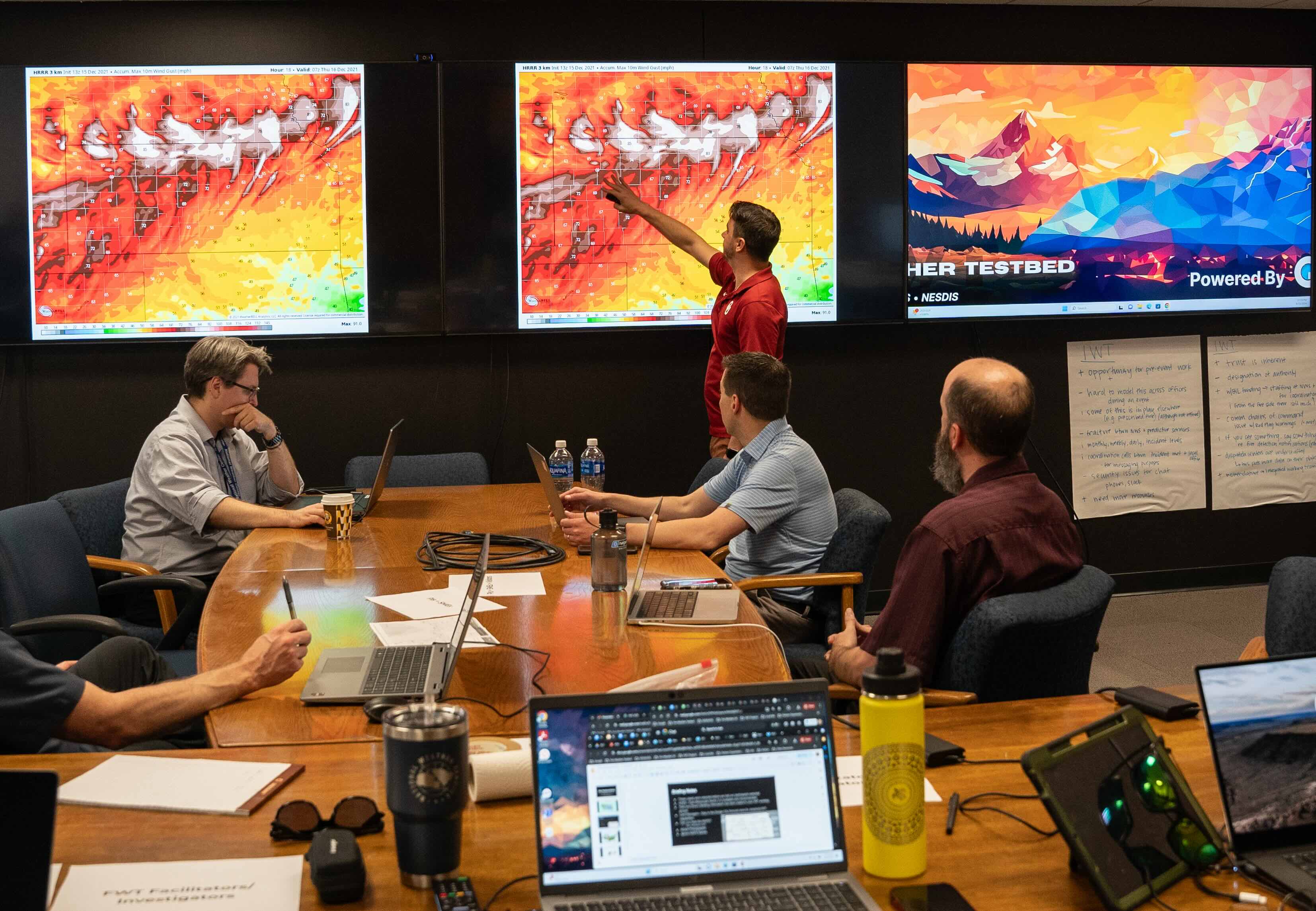 Participants in the NOAA Fire Weather Testbed point out fire weather features on large monitors while others look on.