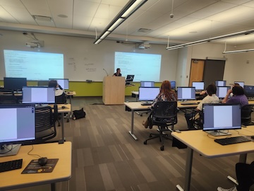 GSL researcher Christina Kumler stands at a podium in front of students at computers during a workshop on using Artificial Intelligence.
